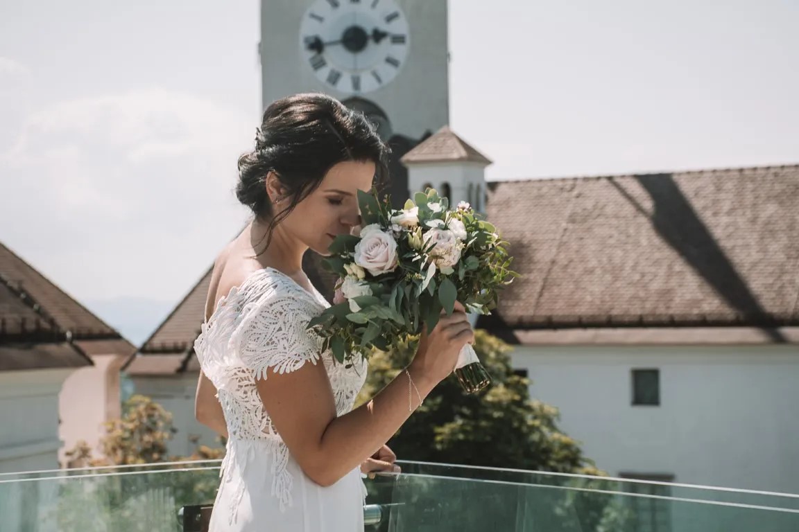 Mladoporočenca na Ljubljanskem gradu v Ljubljani; intimen trenutek ob grajskem obzidju v dokumentarnem poročnem slogu s pogledom na mesto.